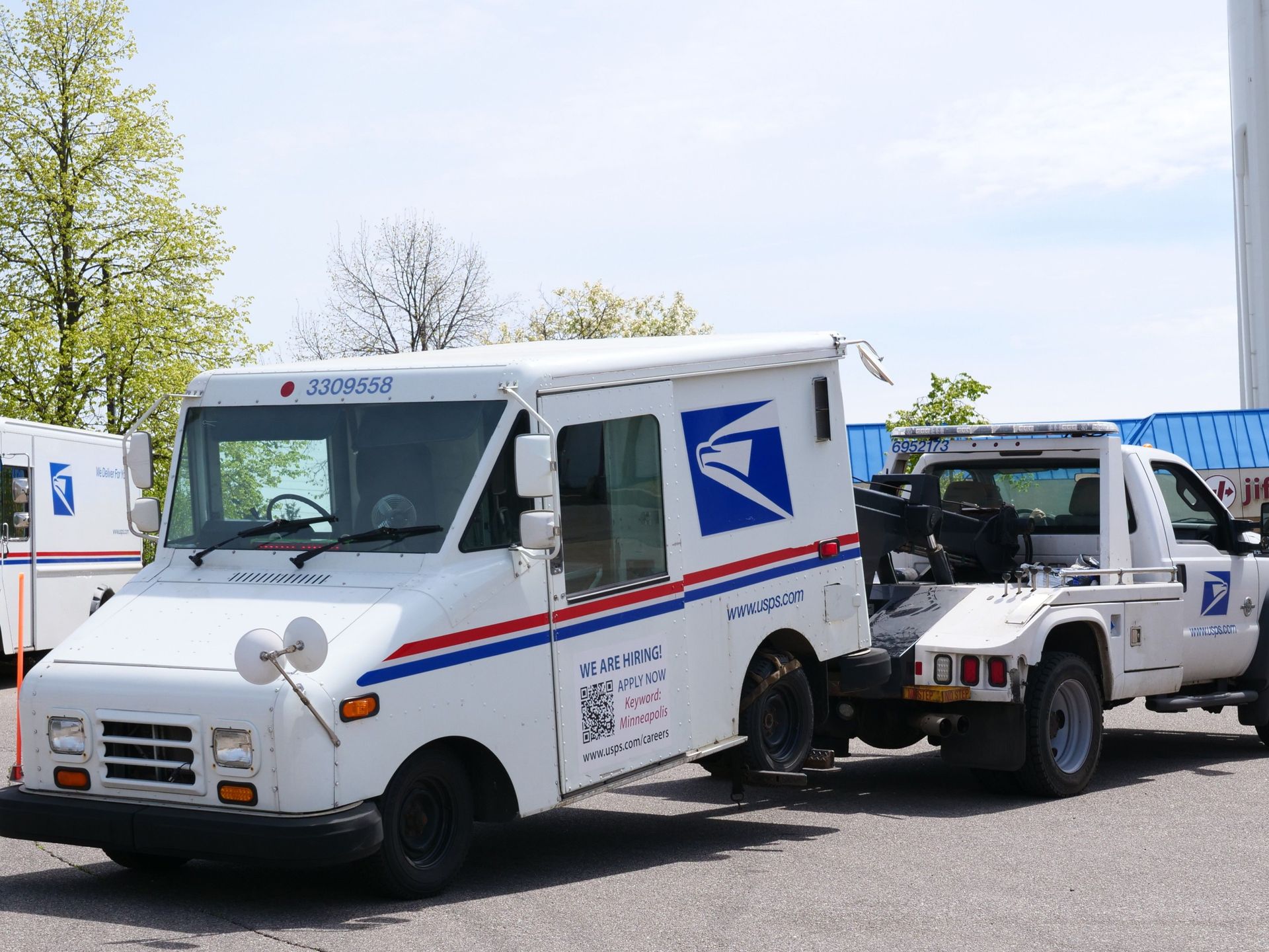 A United States Postal Service (USPS) mail truck is being towed outdoors on a clear day.